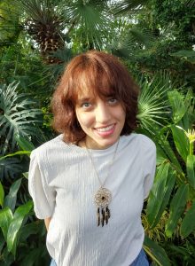 Photo of a brunette woman in a white shirt in front of plants
